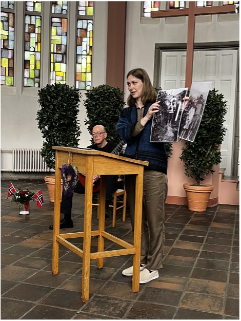 Anna Østby Schippert hält Fotos hoch bei einer Gedenkveranstaltung in der historischen Kapelle XIII des Ohlsdorfer Friedhofs, im Hintergrund Simon Rebstock, 30. Mai 2026